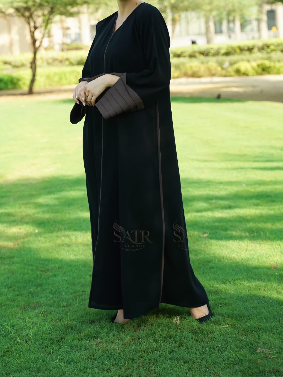 Person wearing a black abaya with 'SATR' branding on a grassy field.
