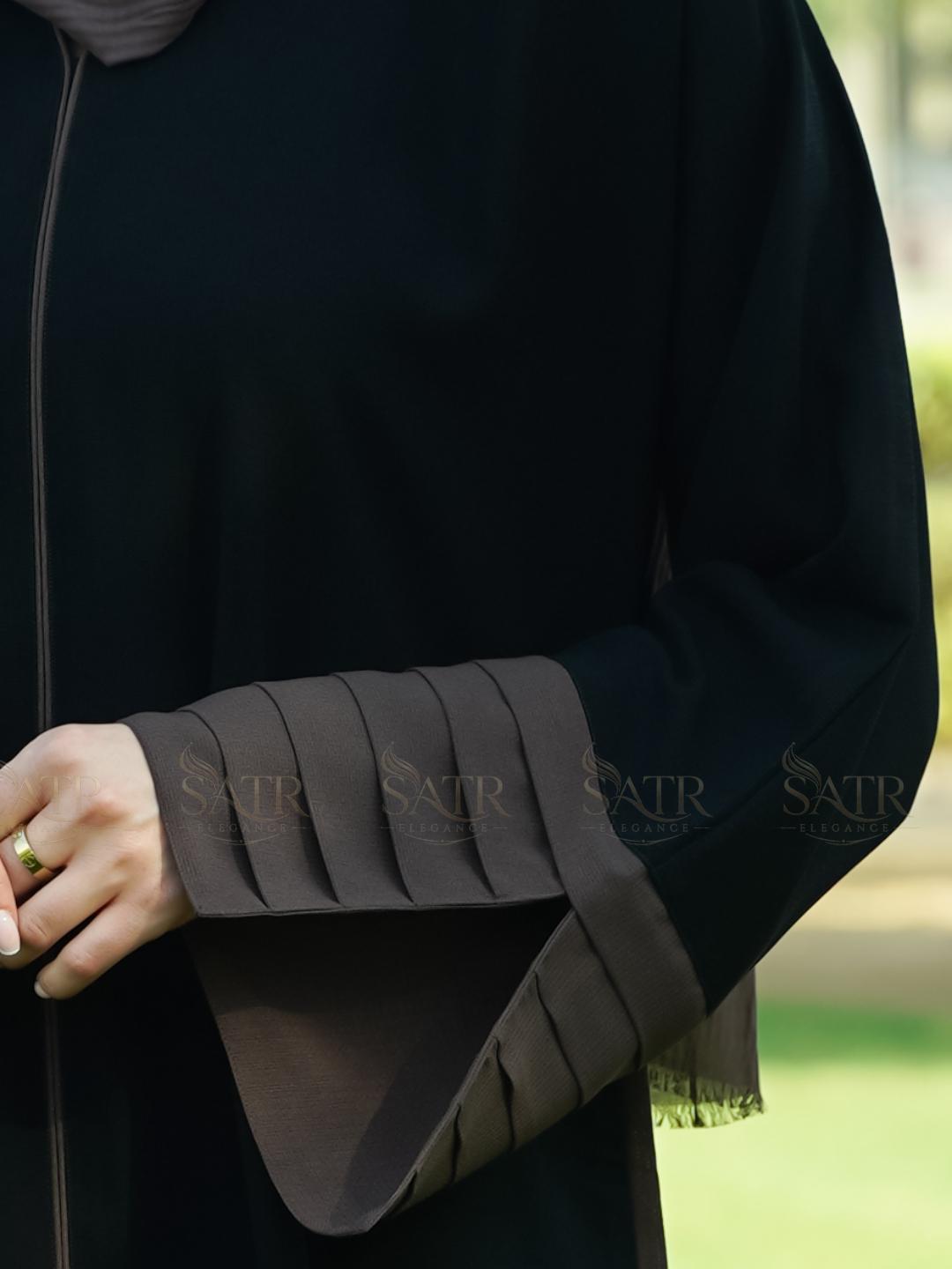 Close-up of a dark abaya with pleated sleeves, brand 'Satr' visible.