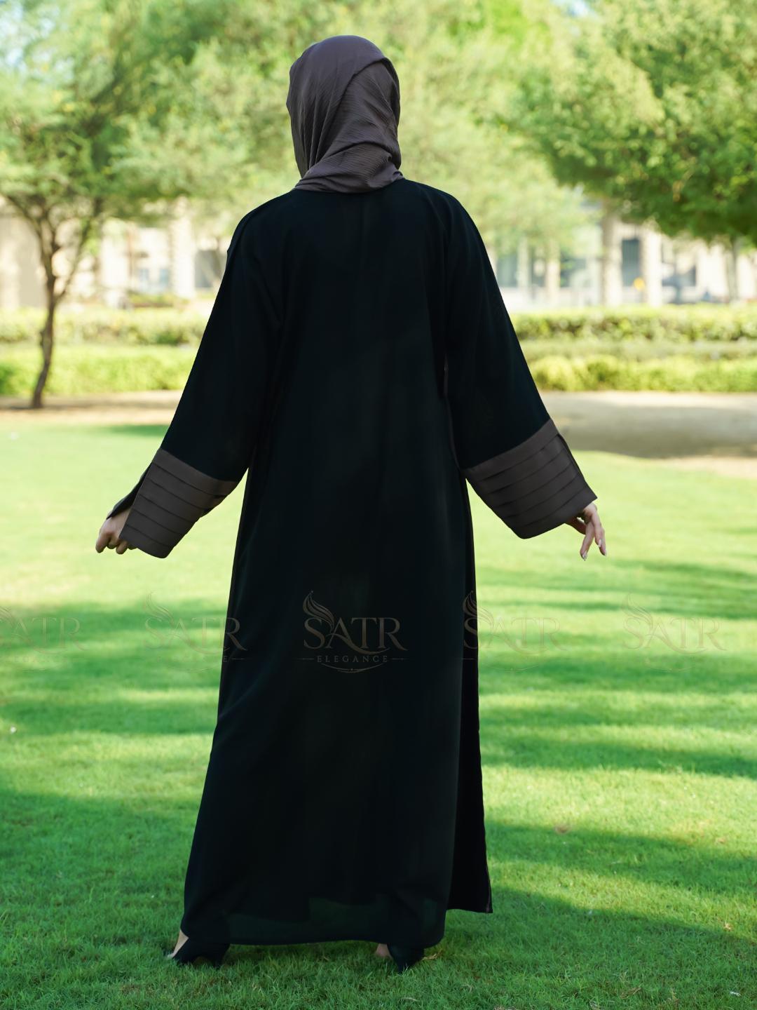 Person wearing a black abaya with 'SATR' branding in an outdoor setting.