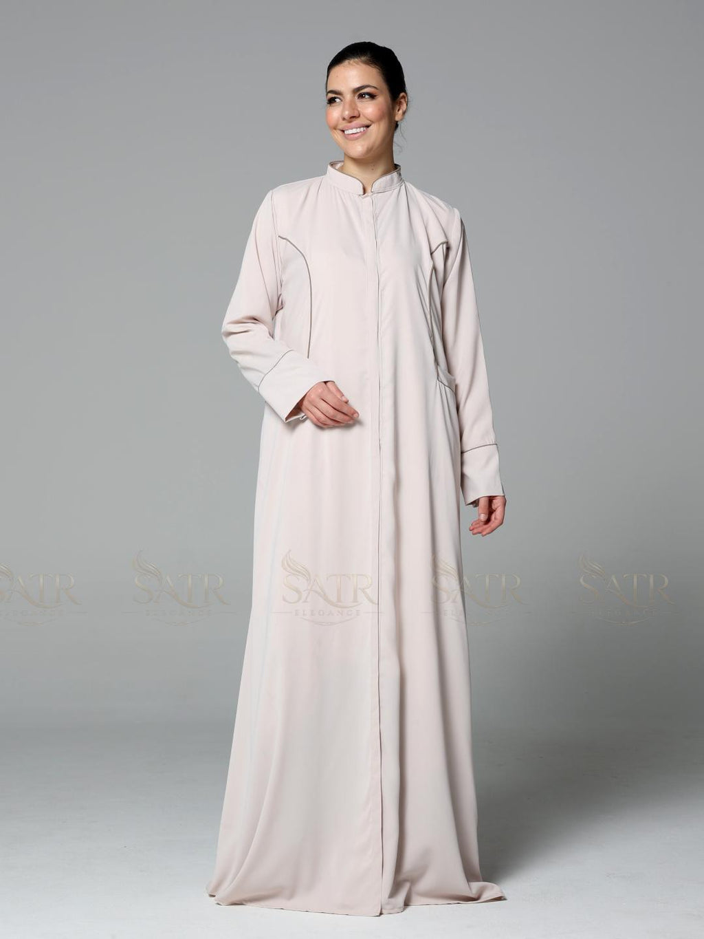 Woman wearing a light pink abaya on a gray background