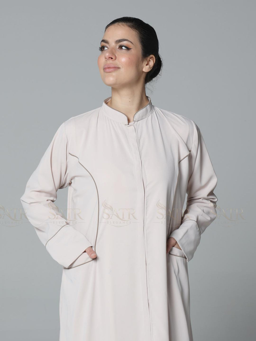 Woman wearing a light-colored long coat against a gray background