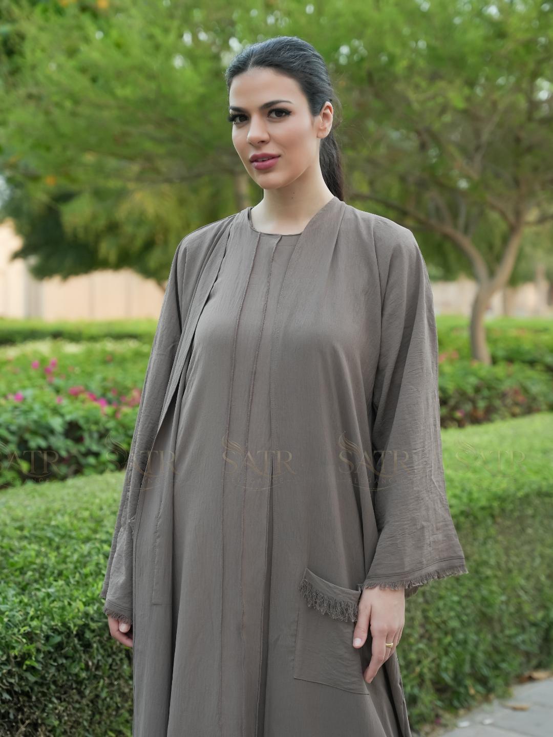 Woman wearing a long, light brown dress with a matching jacket outdoors.