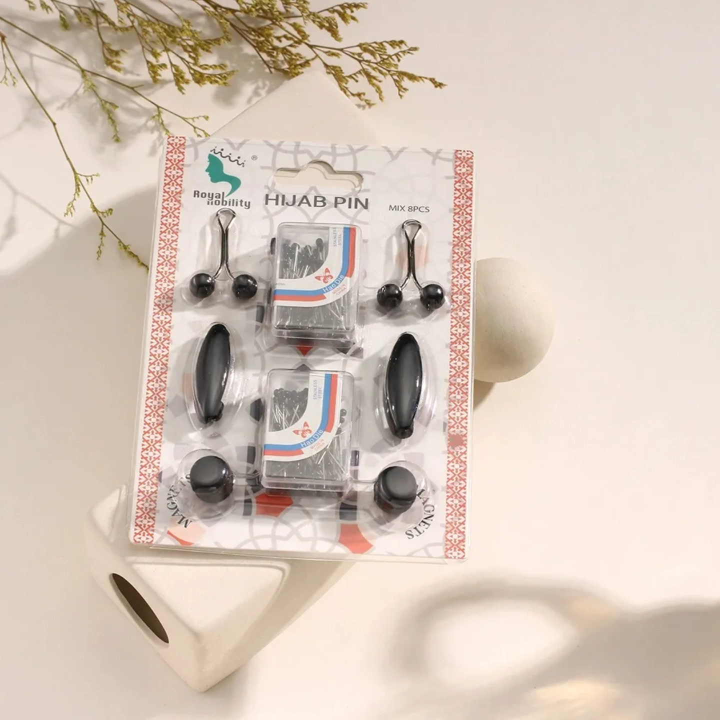 Packaged hijab pins with decorative elements on a light background