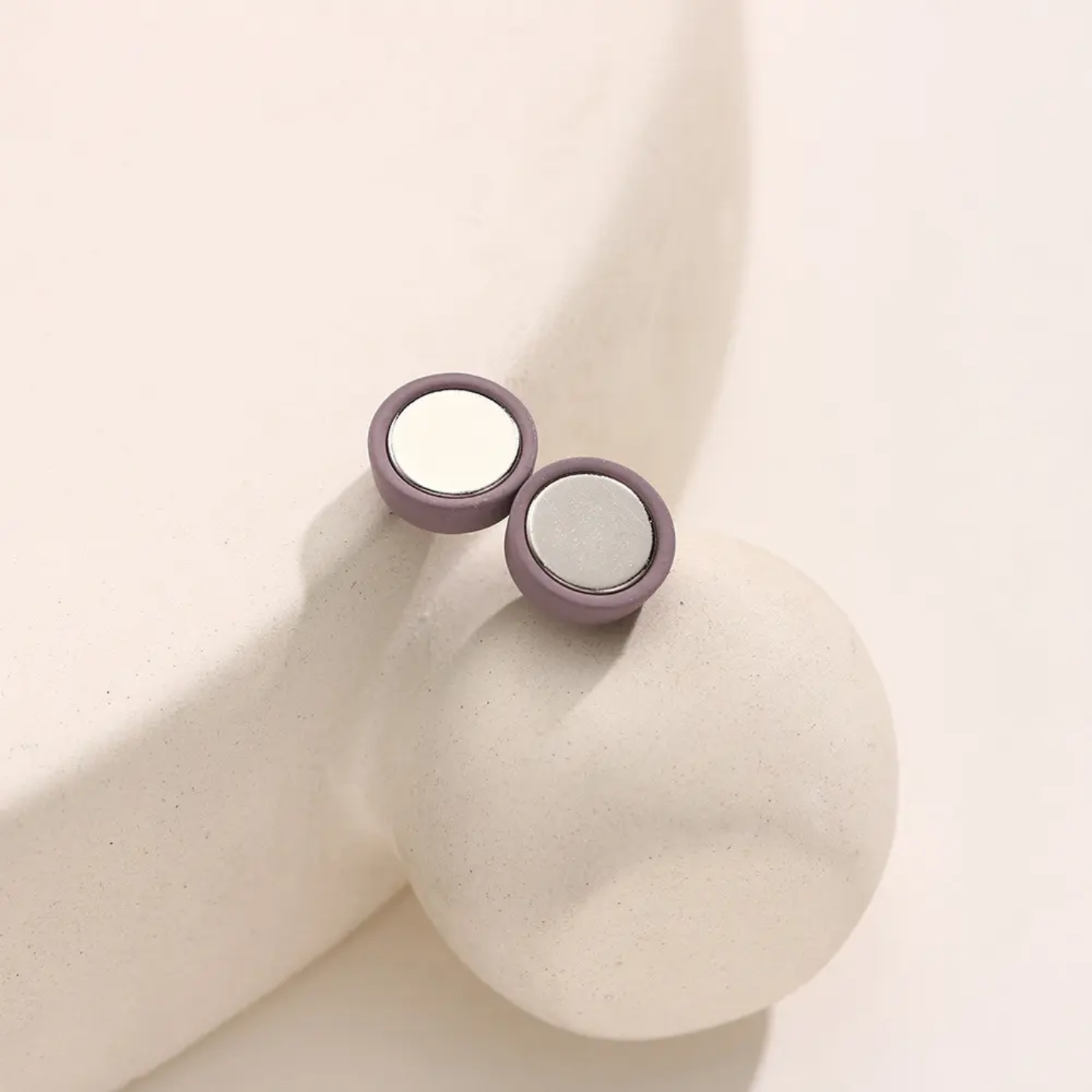 Pair of round magnets with purple and white design on a beige surface